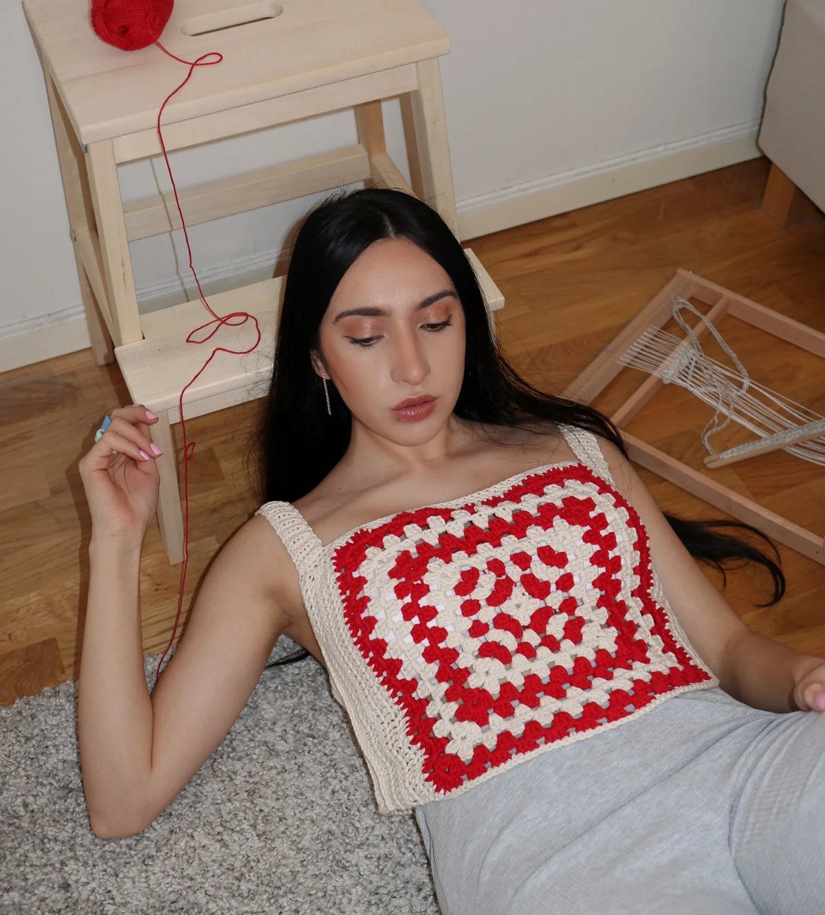 70s Inspired Outfits with 22 Groovy Looks to Try Now 9 Woman lying on a rug wearing a red and white crocheted granny square top.