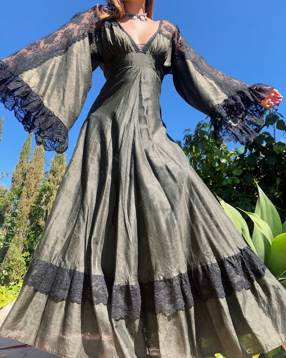 70s Inspired Outfits with 22 Groovy Looks to Try Now 6 A person wearing a long olive green maxi dress with black lace bell sleeves.