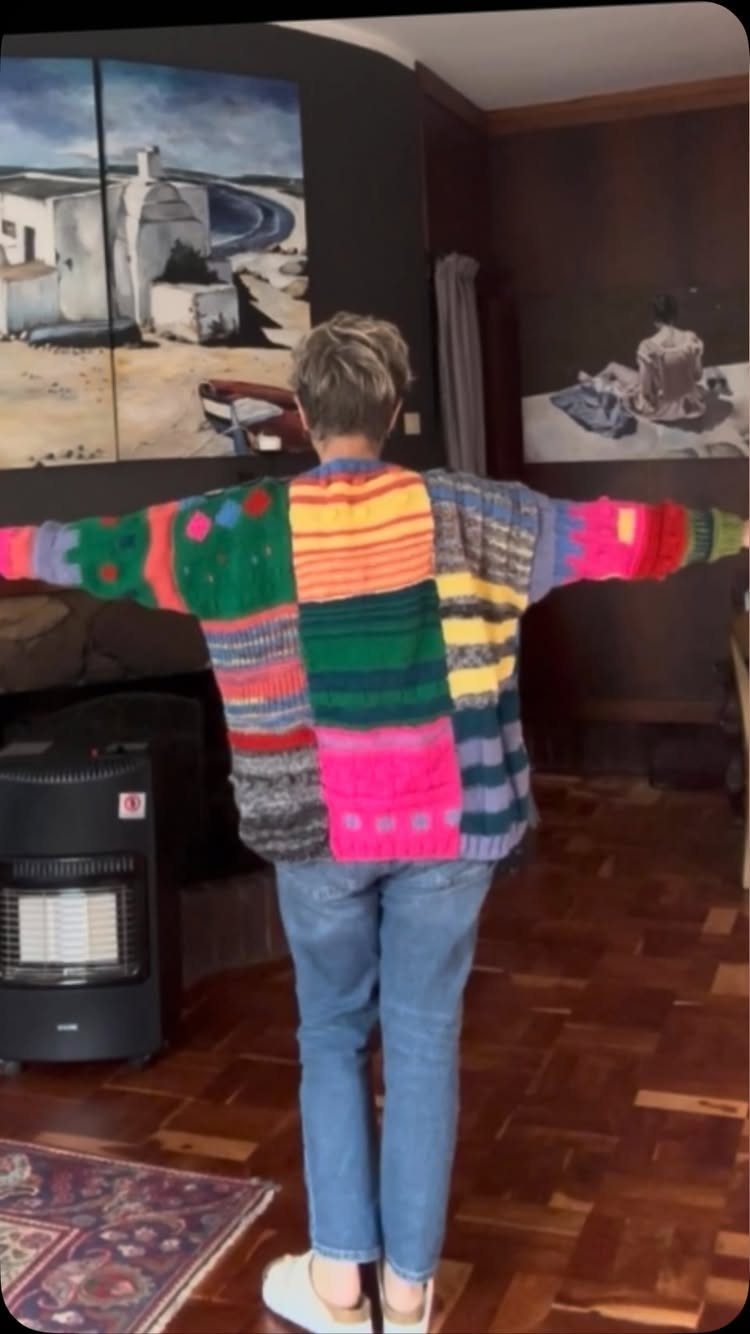 70s Inspired Outfits with 22 Groovy Looks to Try Now 18 Person wearing a vibrant, multi-colored patchwork knit sweater and blue jeans standing in a room.
