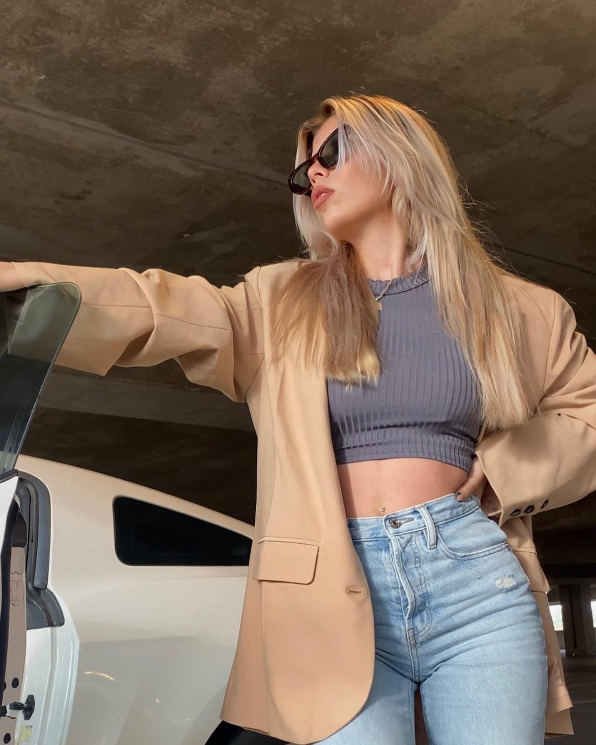 Woman wearing an oversized tan blazer, grey crop top, and light blue jeans.