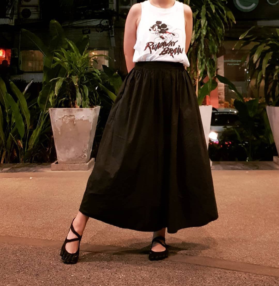 Person wearing a white graphic tank top and a long black midi skirt.
