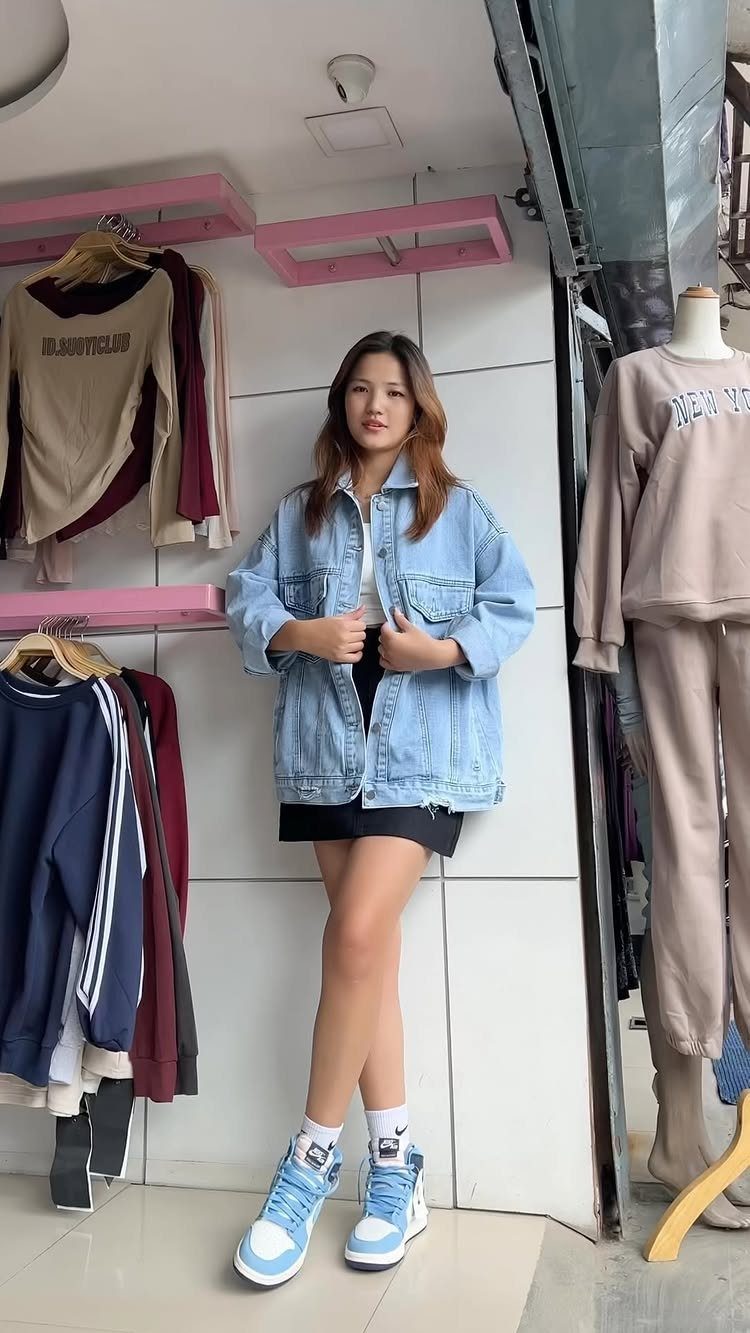 Woman wearing an oversized denim jacket, black mini skirt, and blue high-top sneakers.