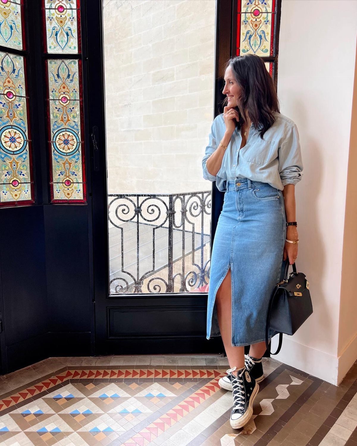 Woman wearing a light blue shirt, long denim skirt, and black high-top sneakers.