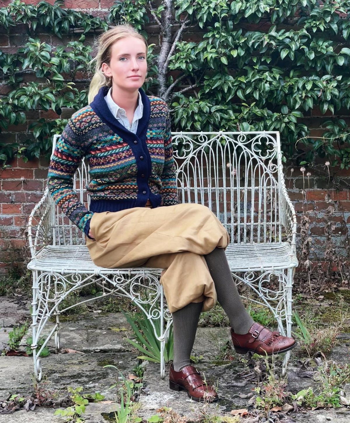 Woman wearing a Fair Isle cardigan and tan corduroy pants sitting on a bench.