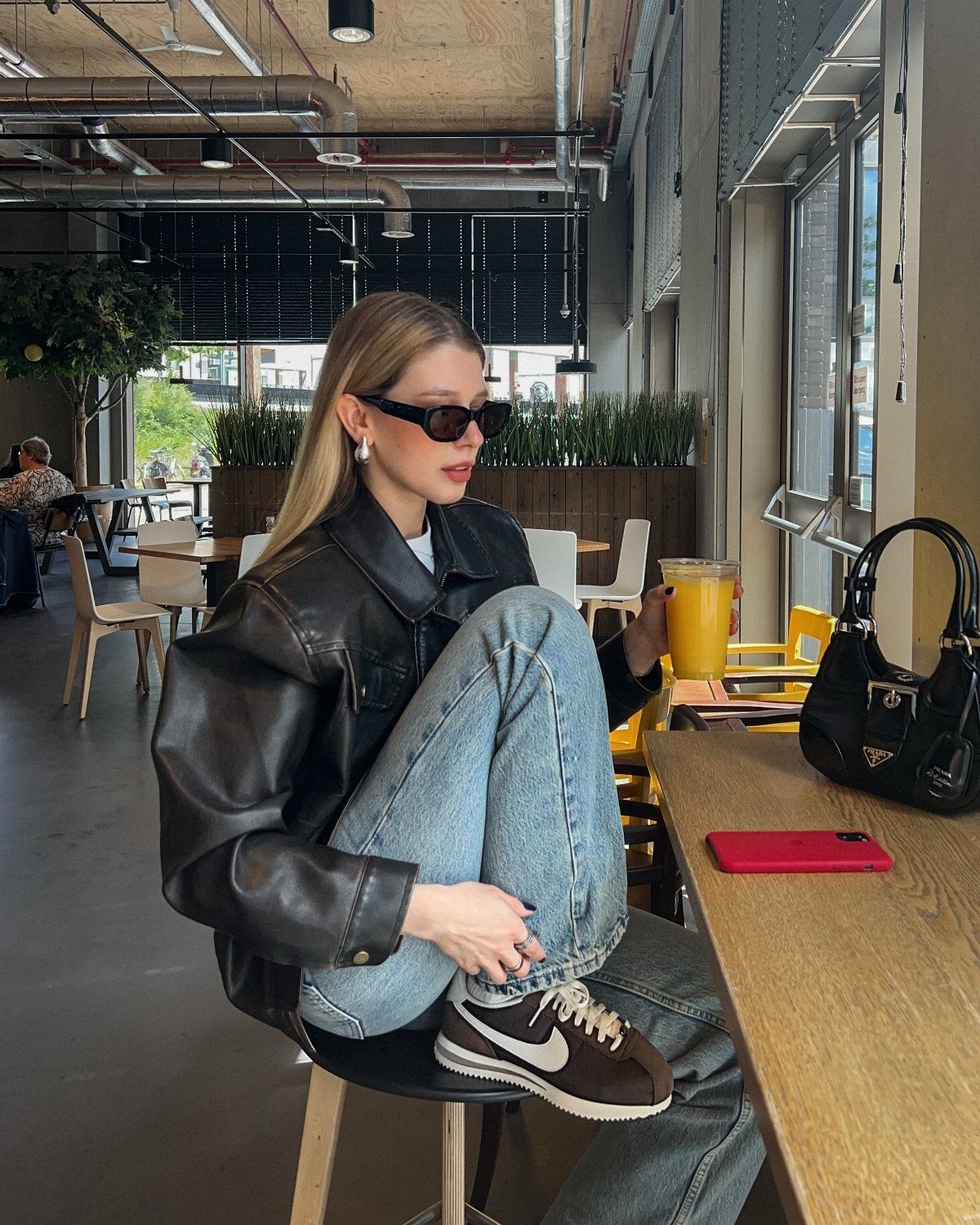 Woman in black leather jacket and blue jeans sitting in a modern cafe.