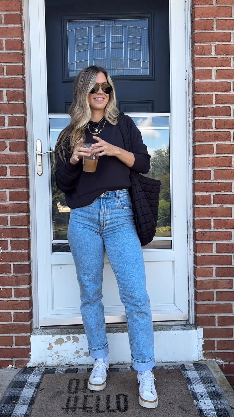 Woman wearing high-waisted light blue mom jeans and a black sweater standing by a door.