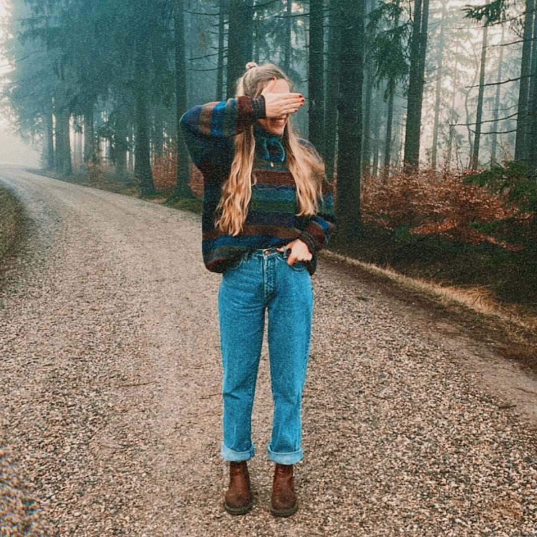 Woman in oversized striped knit sweater and blue jeans on a foggy forest path.