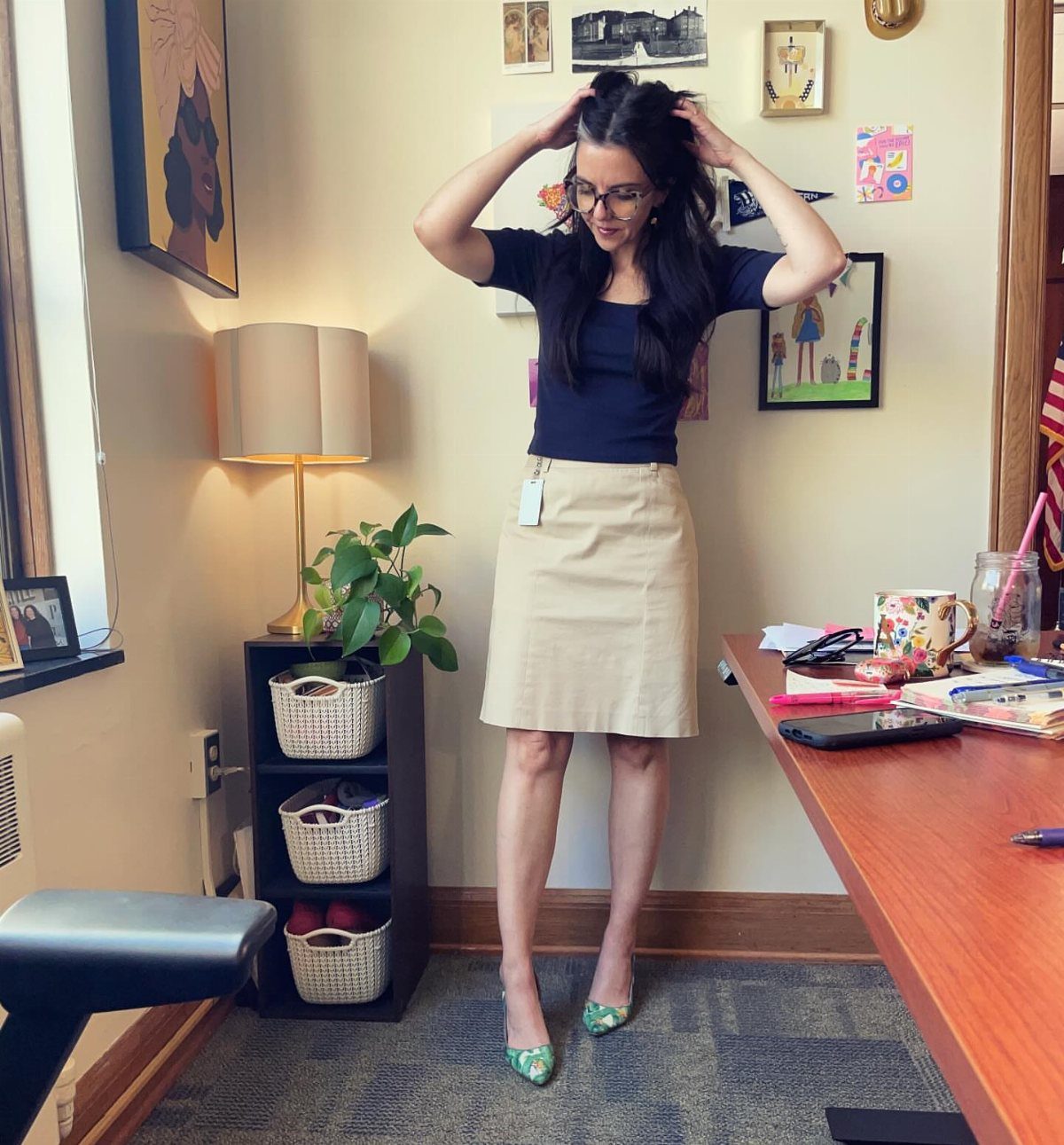 Woman wearing a black top and beige pencil skirt in a home office.