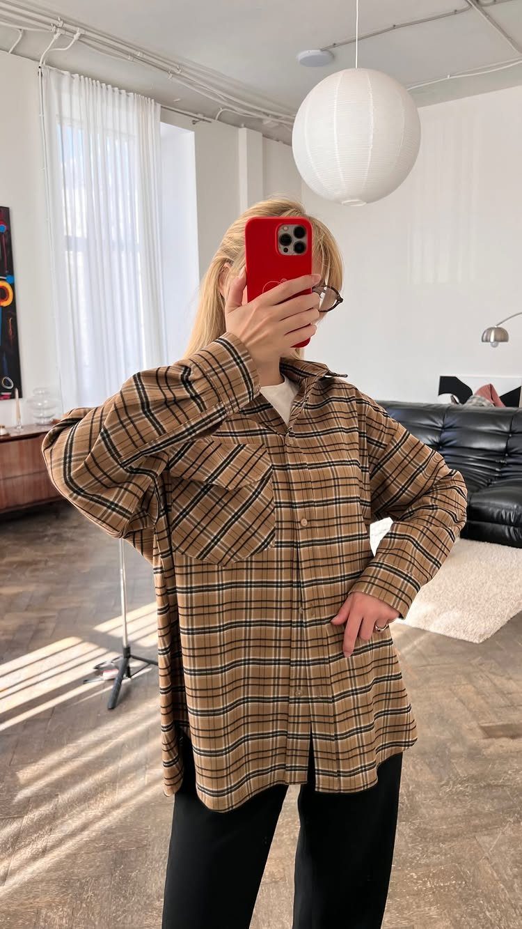 Person wearing an oversized brown plaid shirt and black trousers in a bright room.
