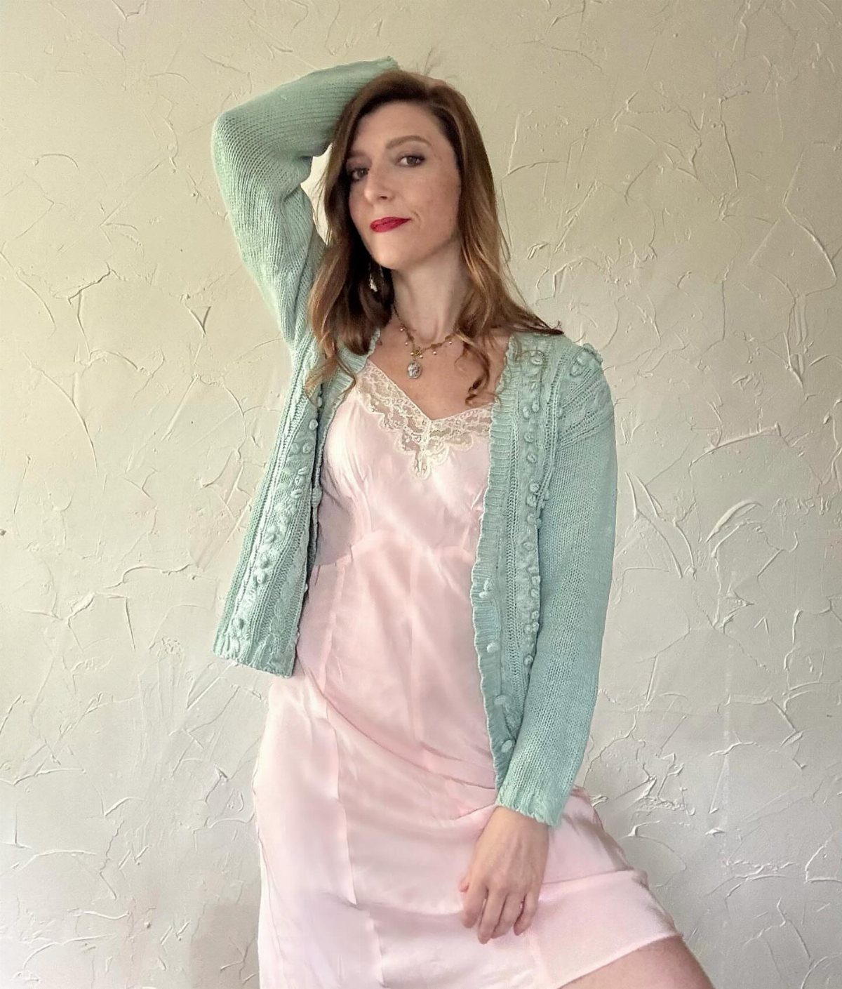 Woman wearing a pink satin slip dress and a light blue knit cardigan.