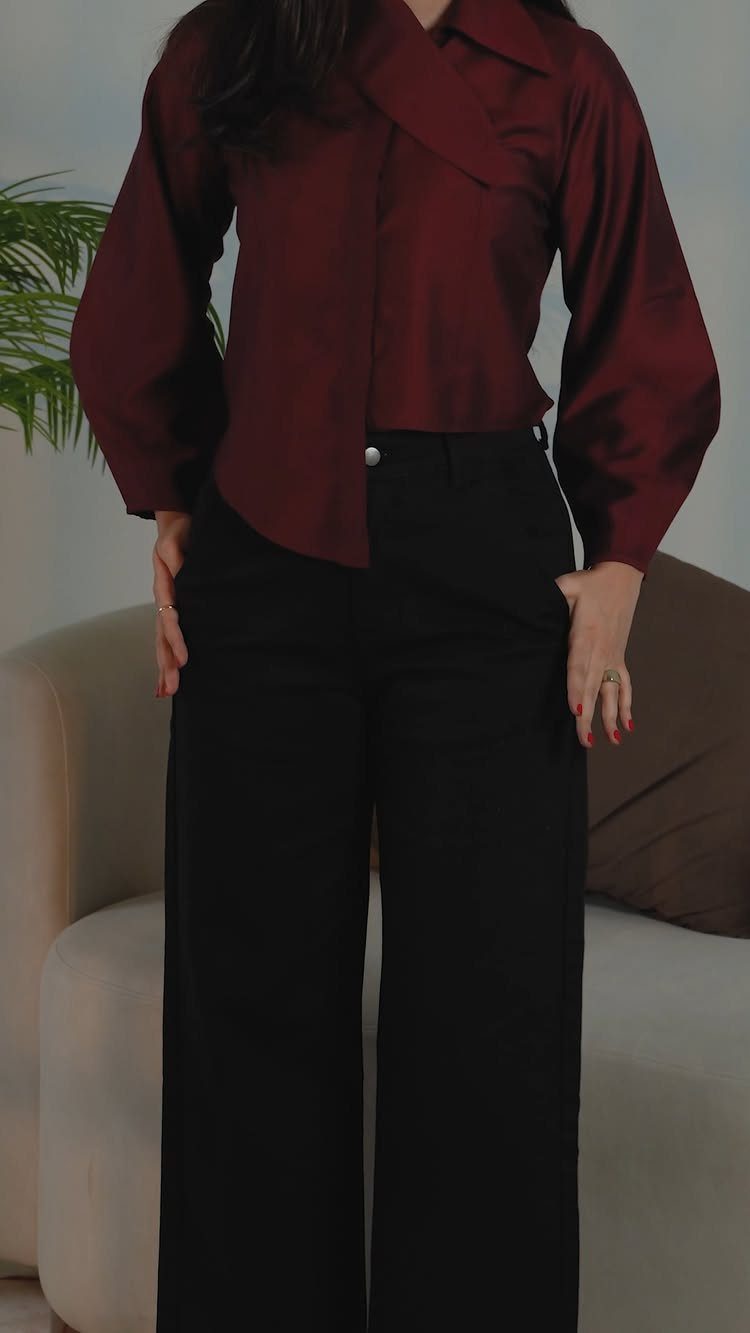Person wearing a maroon long-sleeved shirt and wide-leg black trousers indoors.