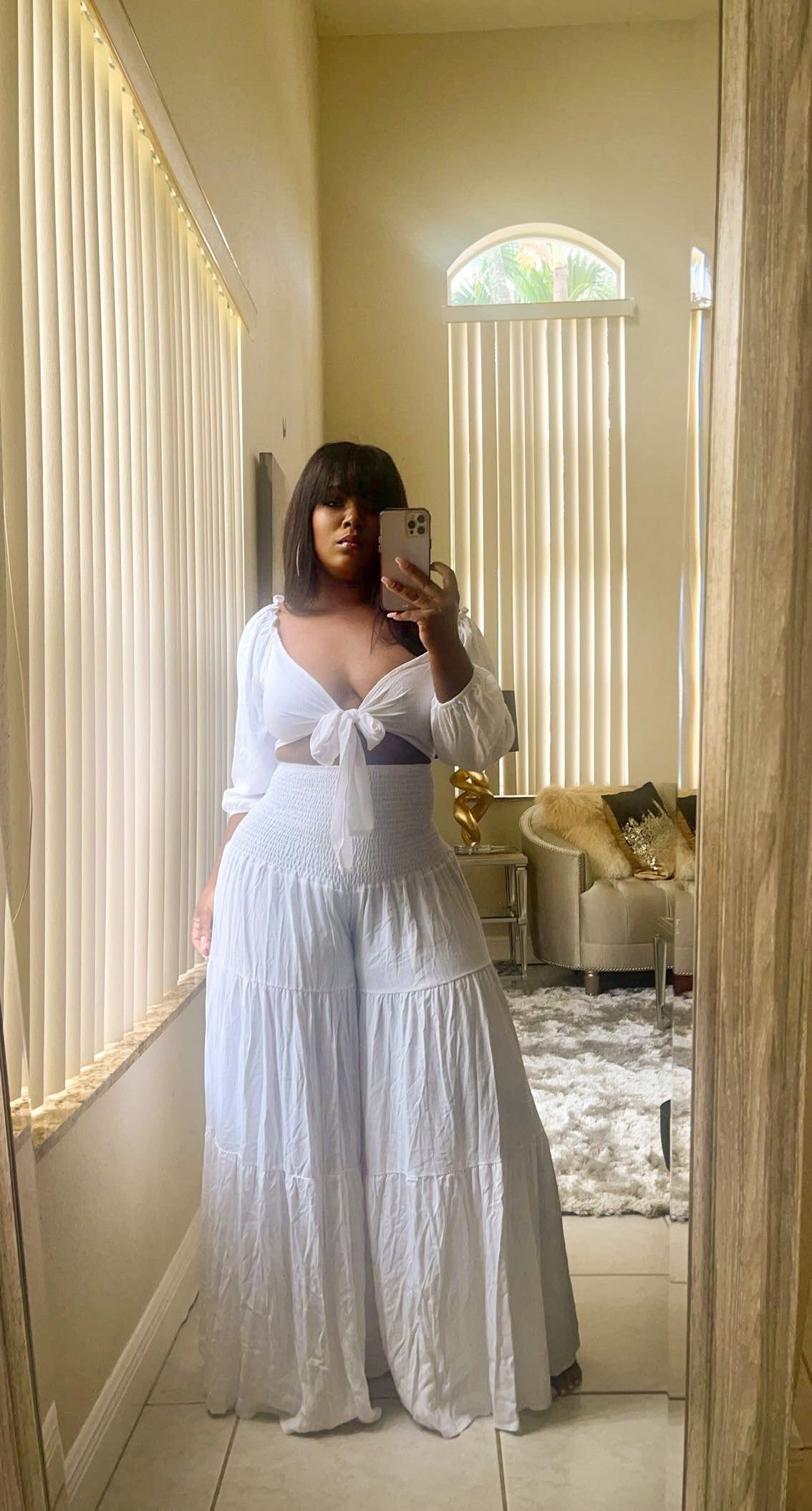 Woman in white off-the-shoulder top and high-waisted wide-leg trousers posing for a mirror selfie.