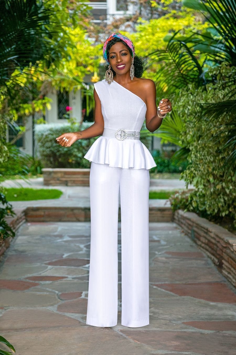 Woman posing in a white one-shoulder peplum top and wide-leg trousers in a garden.