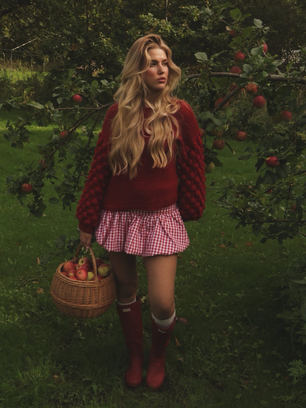 Apple Picking Outfit Ideas: 12 Looks for the Orchard 2 Woman in red sweater and gingham skirt holding apple basket in orchard