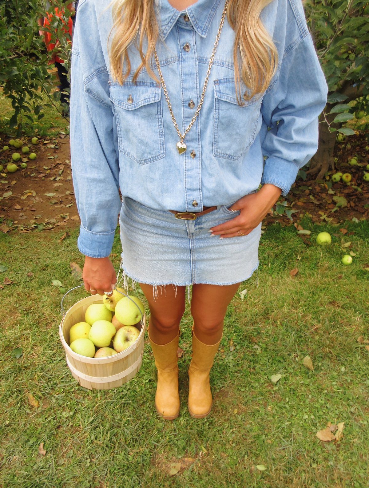 Apple Picking Outfit Ideas: 12 Looks for the Orchard 12 Person in denim outfit holding a bucket of green apples in an orchard.
