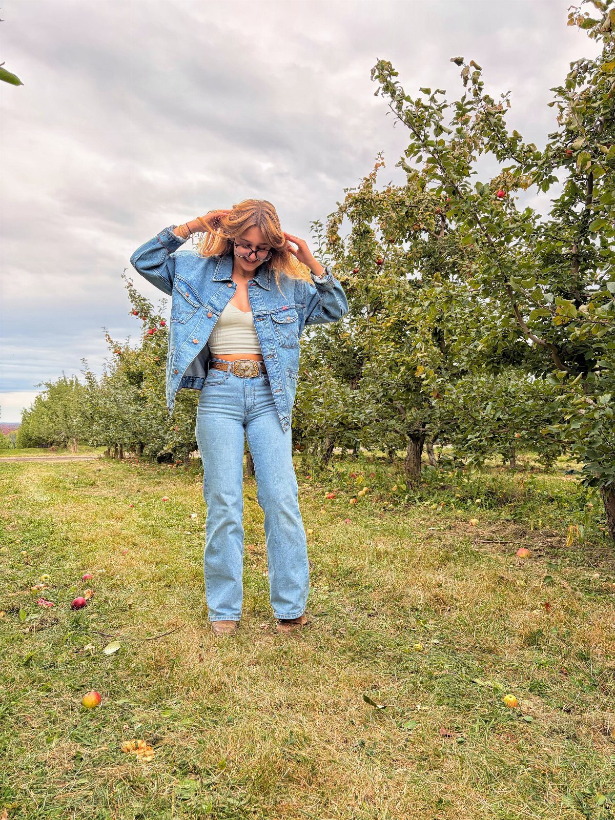 Apple Picking Outfit Ideas: 12 Looks for the Orchard 5 Woman wearing a cropped denim jacket and wide-leg jeans in an apple orchard.