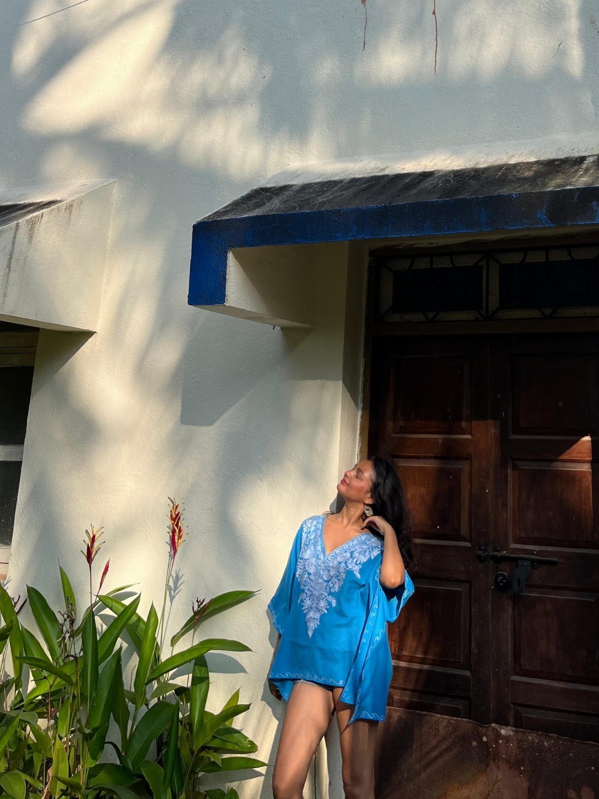 Beach Vacation Outfits: 9 Ideas for Easy Packing 2 Woman in a blue embroidered kaftan standing by a white wall and wooden door.