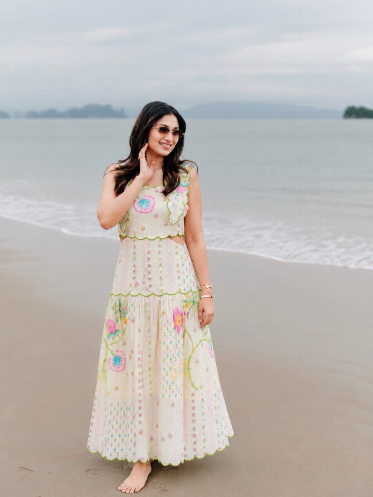 Beach Vacation Outfits: 9 Ideas for Easy Packing 4 Woman in a white floral embroidered maxi dress standing on a sandy beach by the ocean.