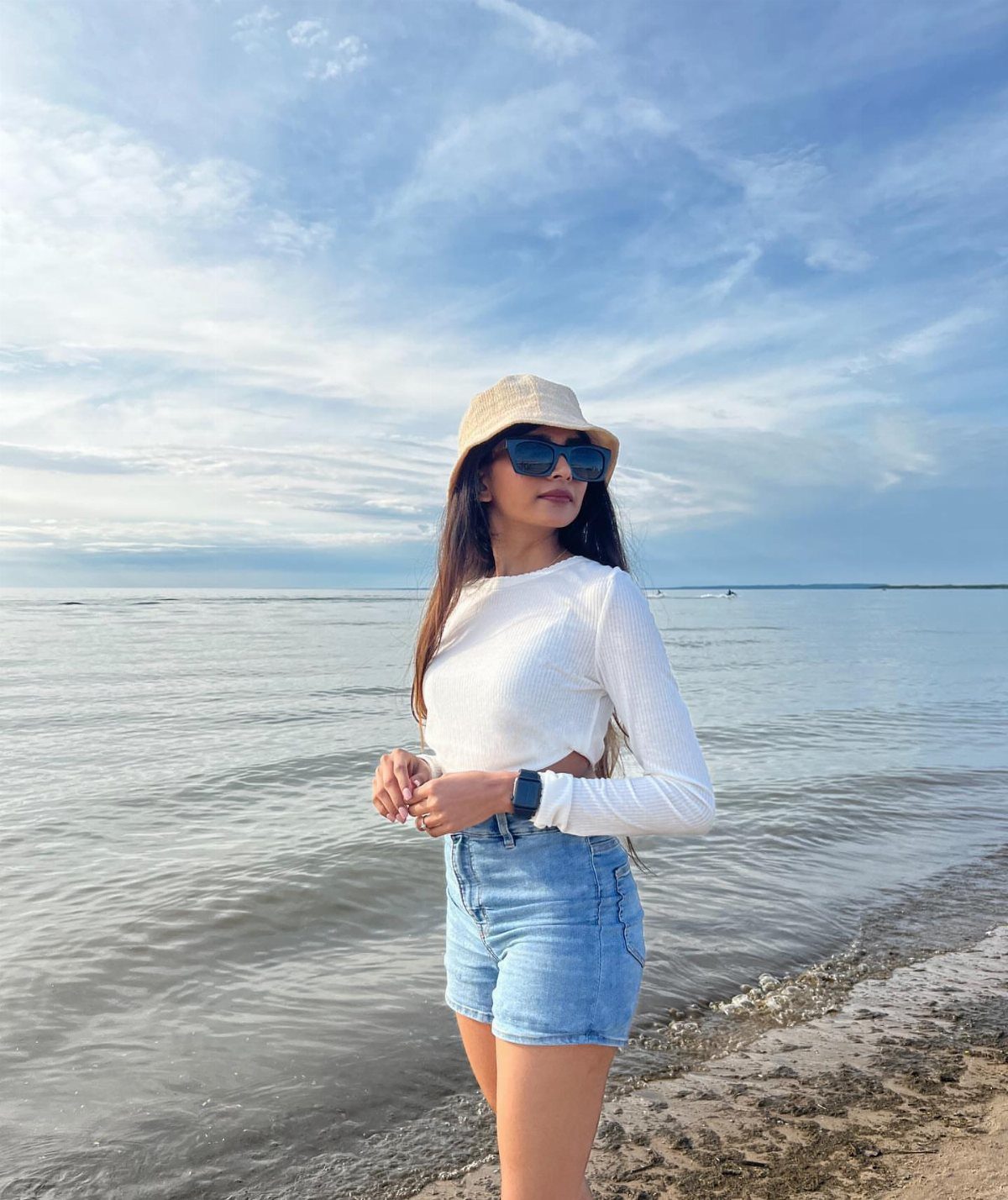 Beach Vacation Outfits: 9 Ideas for Easy Packing 7 Woman in white crop top and denim shorts posing on a beach.
