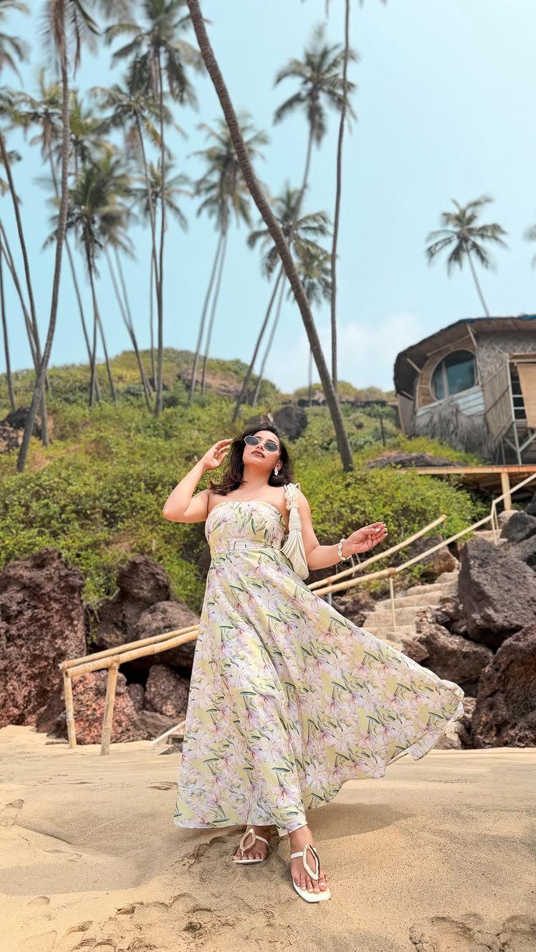 Beach Vacation Outfits: 9 Ideas for Easy Packing 1 Woman in a flowing tropical-print maxi dress posing on a sandy beach with palm trees.