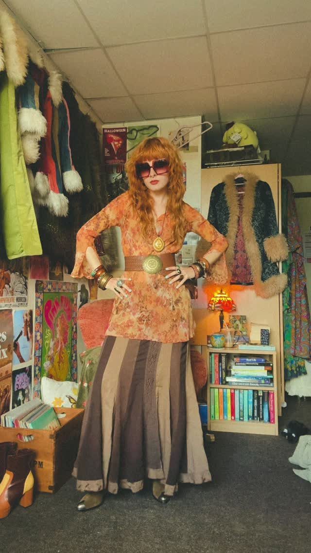 A woman posing in a bohemian-style orange tunic and long striped skirt.