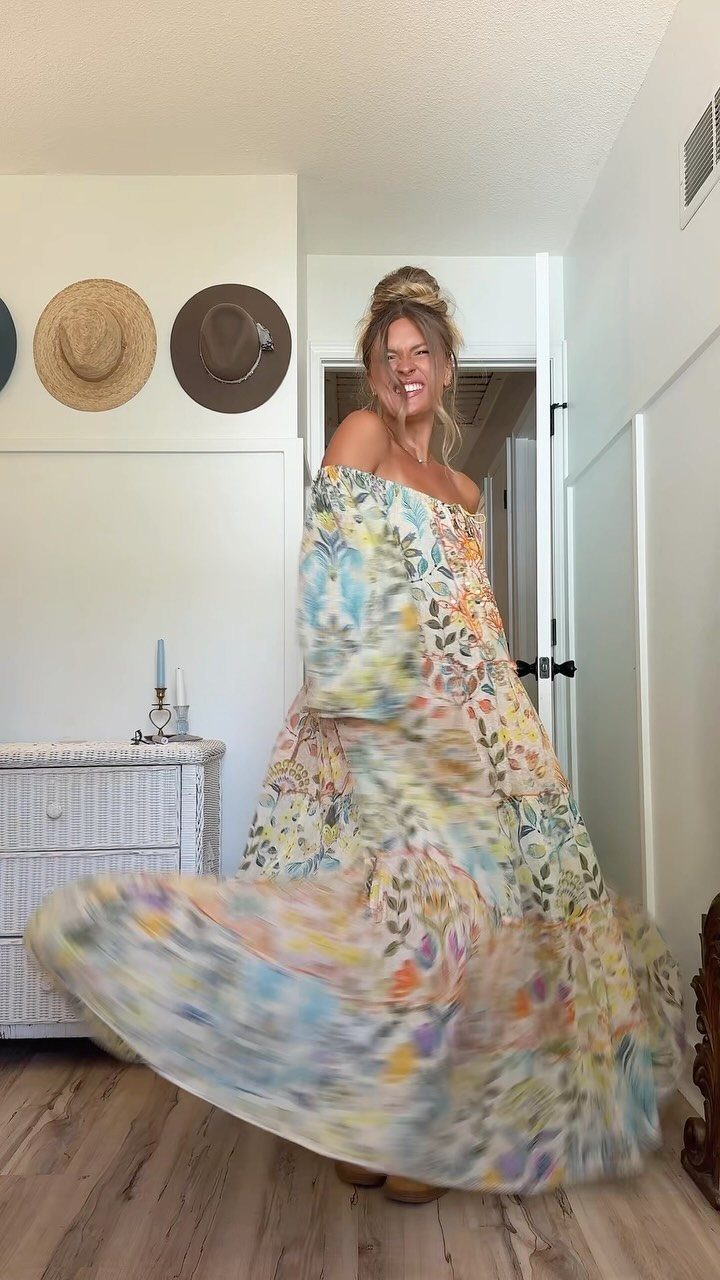 A woman twirling in a colorful floral print off-the-shoulder maxi dress.