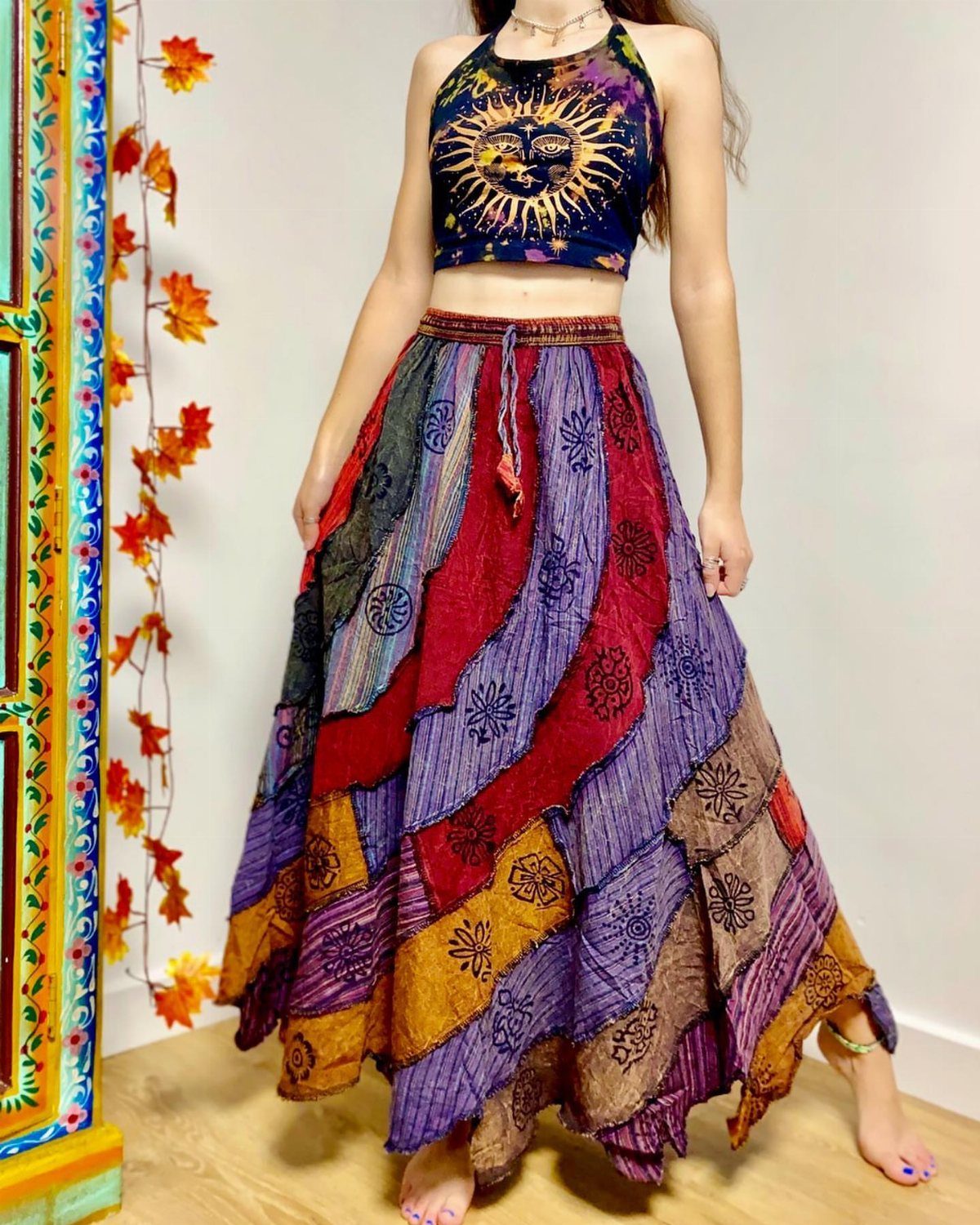 A person wearing a sun-patterned crop top and a colorful patchwork maxi skirt.