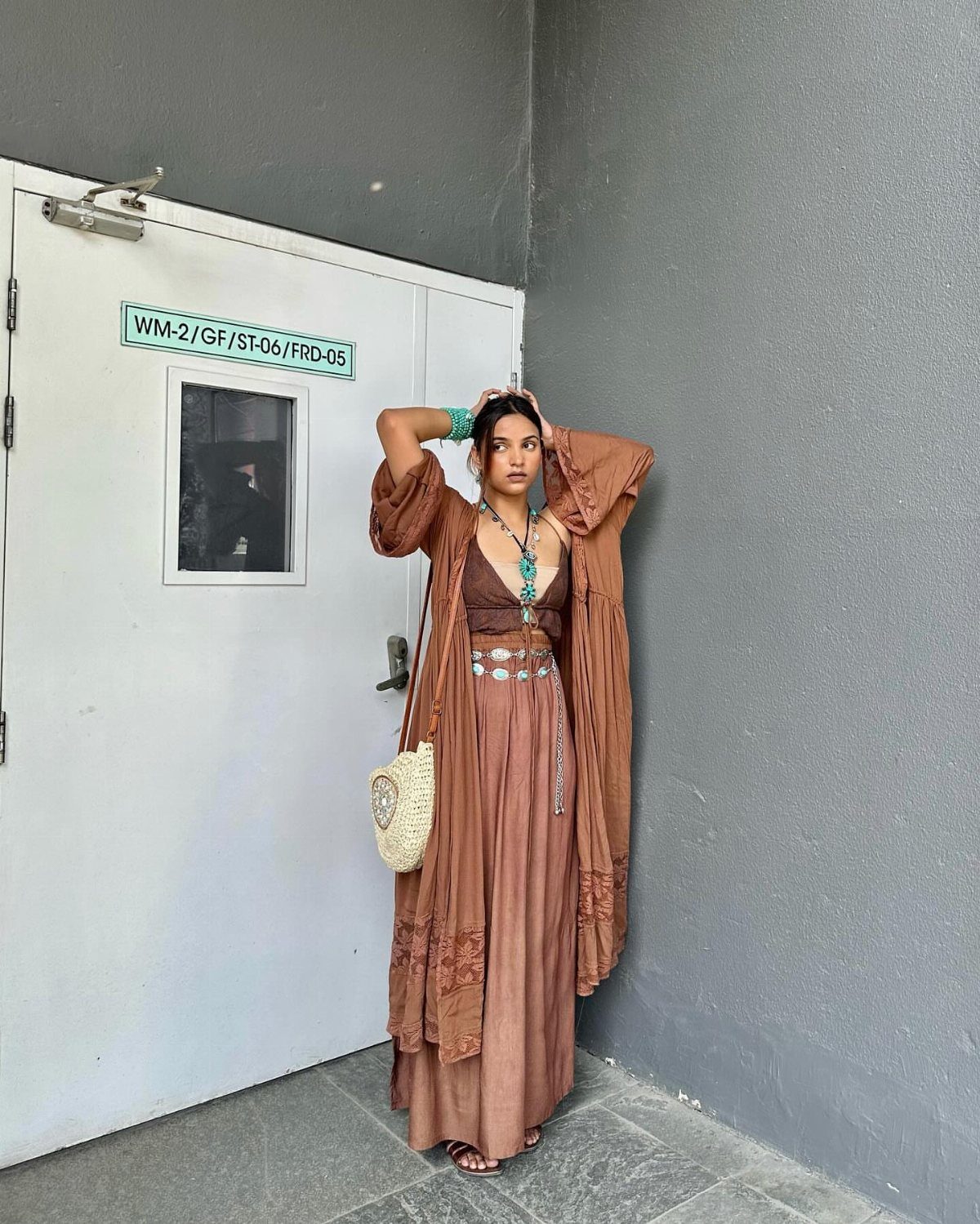 Woman in a burnt sienna maxi dress and duster posing against a grey wall.