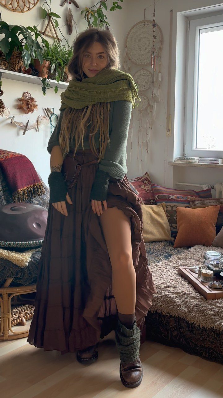 Woman with dreadlocks wearing a green top, large scarf, and long brown tiered skirt in a bohemian room.