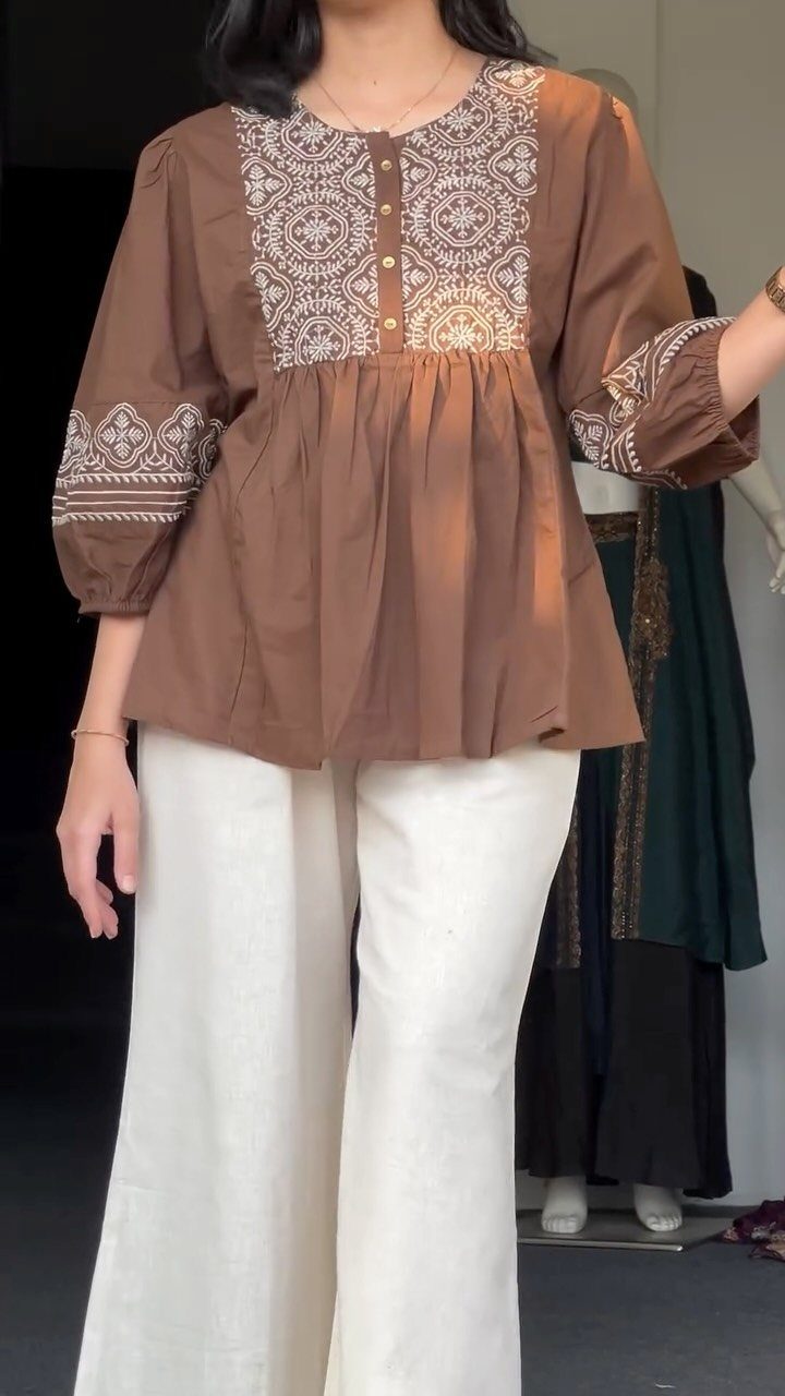 Person wearing a brown embroidered blouse and wide-leg white trousers.