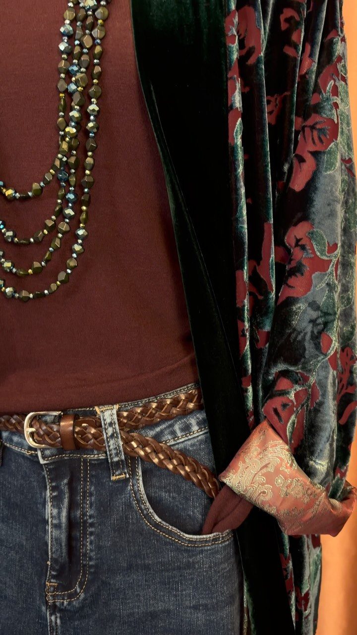 Person wearing a brown top, blue jeans, braided belt, beaded necklaces, and a floral velvet robe.