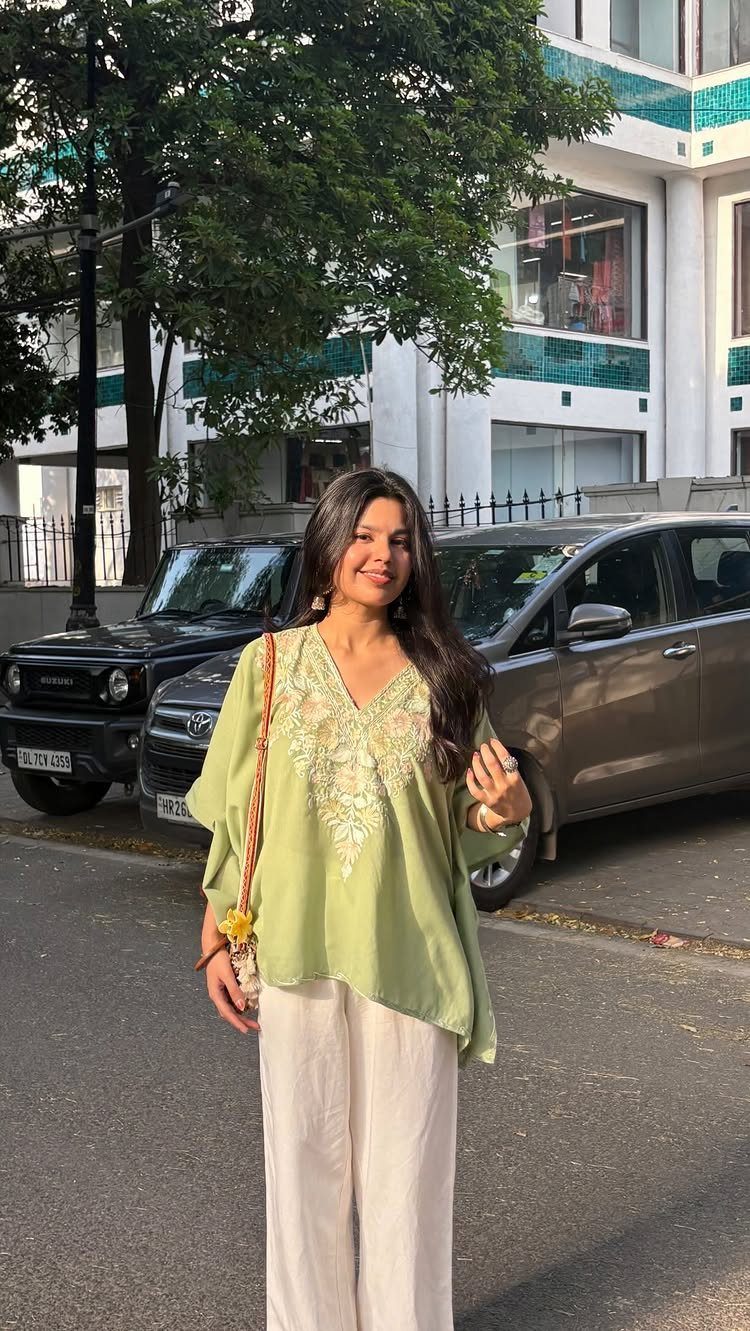 Woman posing in a green embroidered tunic and cream wide-leg trousers on a city street.