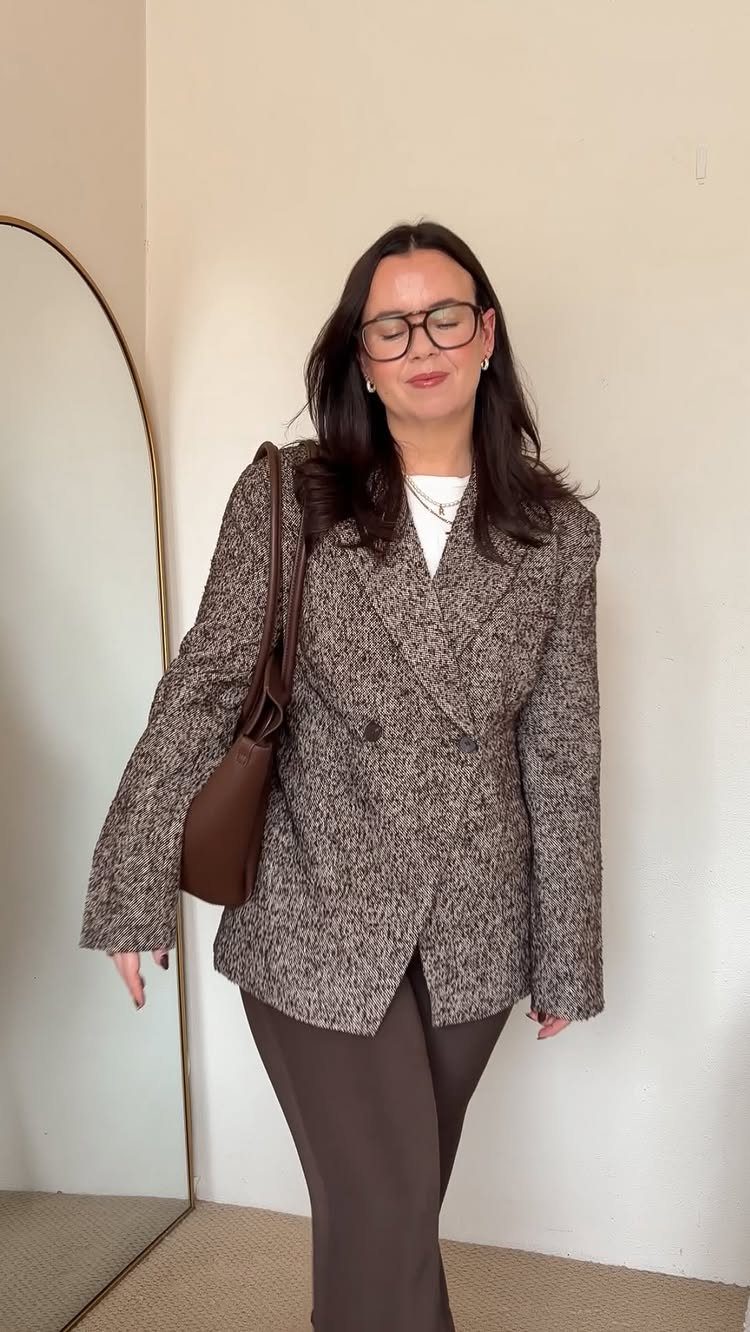 Business Casual Outfits for Work: 8 Polished Ideas 1 Woman wearing a textured brown tweed blazer and dark brown trousers standing near a mirror.