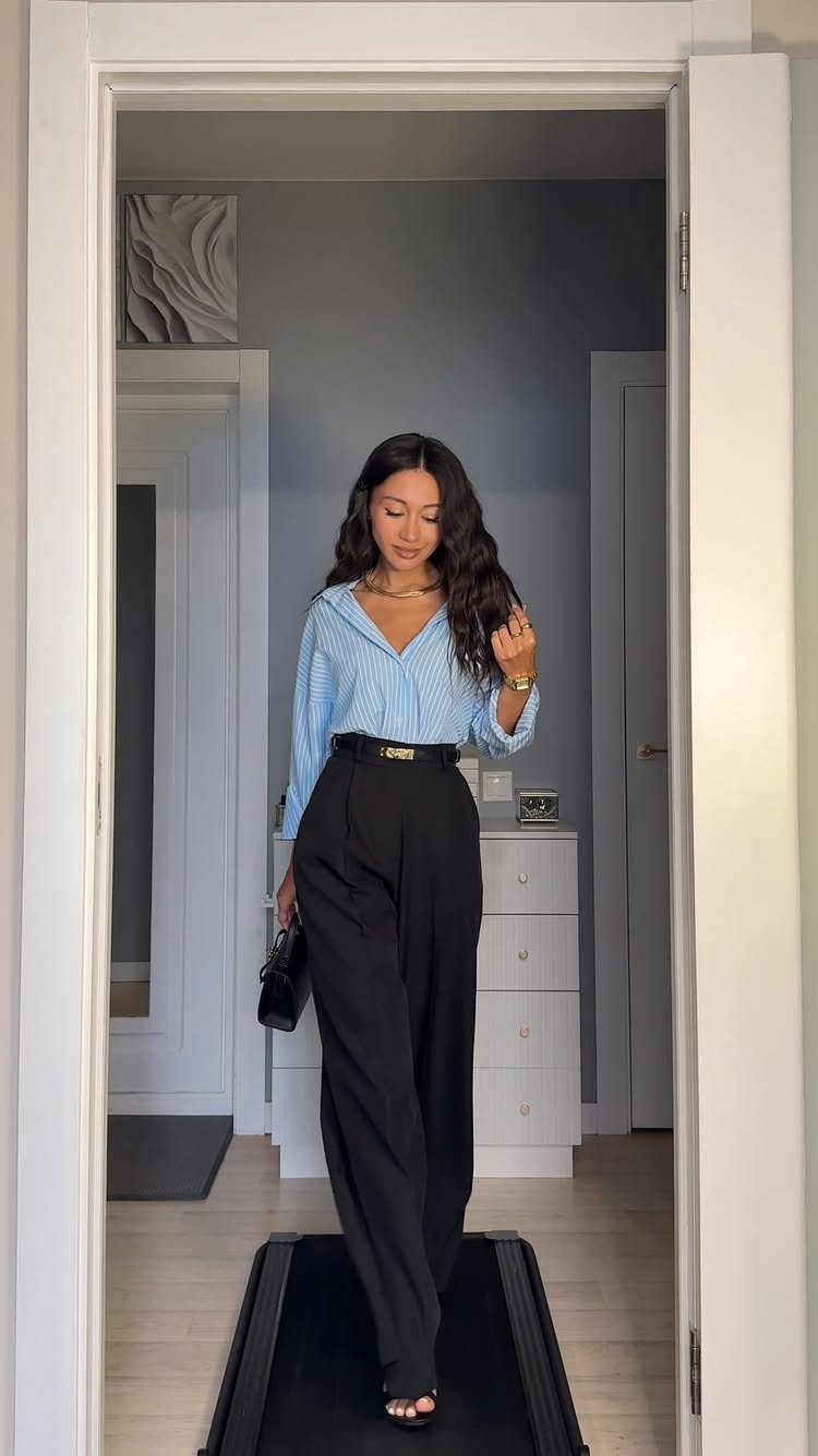 Business Casual Outfits for Work: 8 Polished Ideas 6 Woman in a blue striped shirt and black high-waisted trousers standing in a doorway.