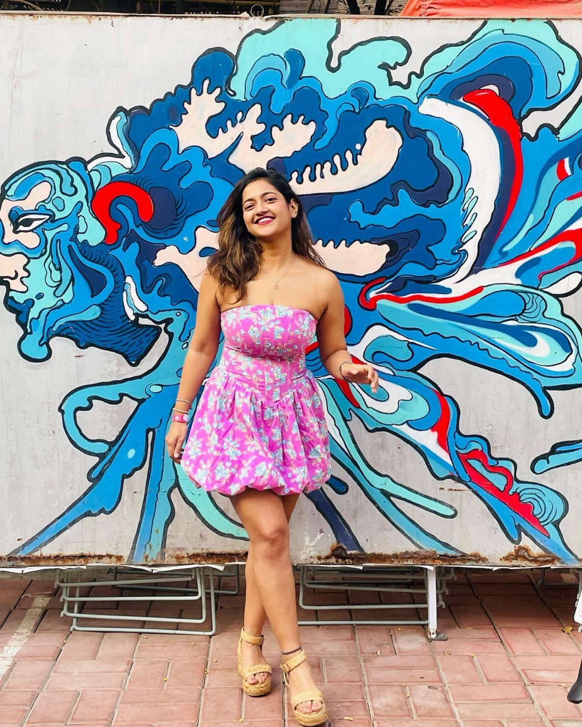 Woman in a pink floral mini dress and platform sandals posing by graffiti.