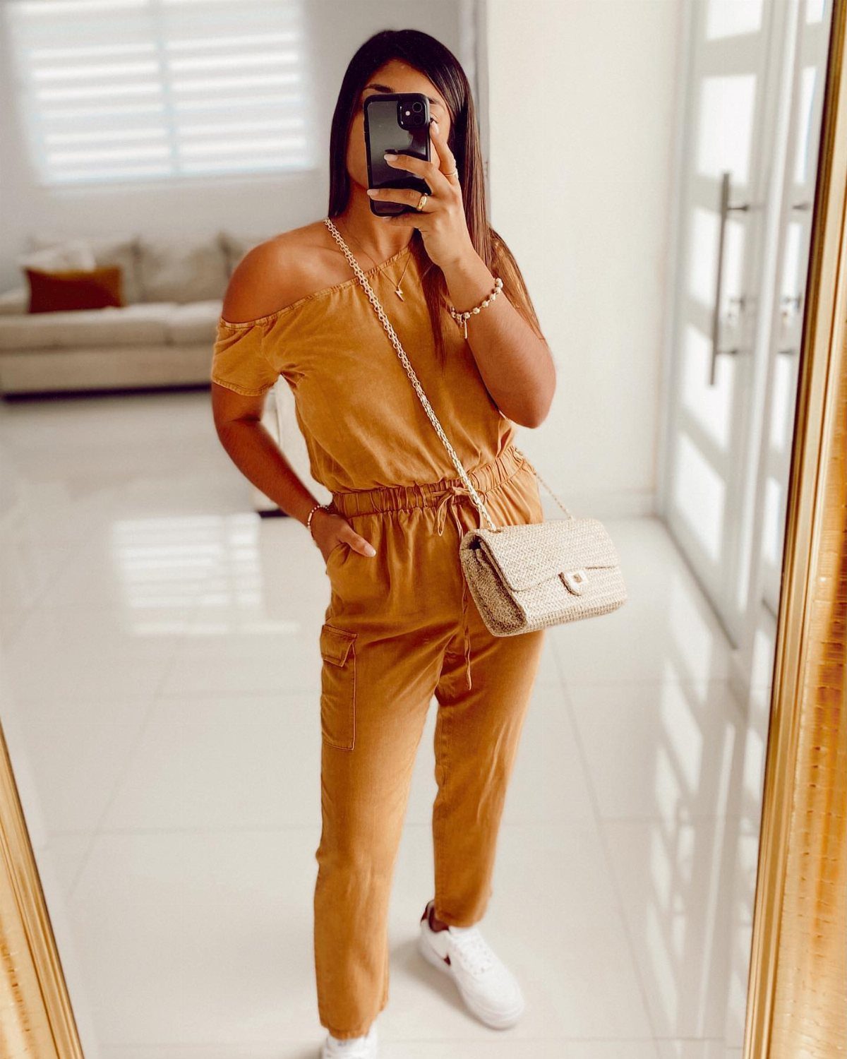 Woman in mustard yellow jumpsuit with white sneakers and a small beige crossbody bag.
