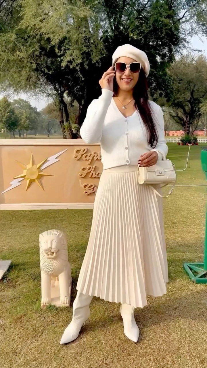 Woman in white knit cardigan and pleated midi skirt wearing a white beret.