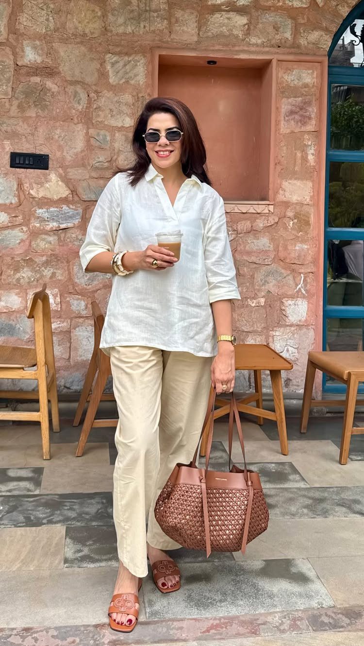 Woman wearing a white linen shirt and beige linen pants holding a coffee cup.