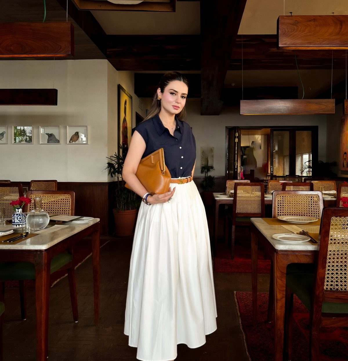 Woman in navy top and white maxi skirt posing in a restaurant setting