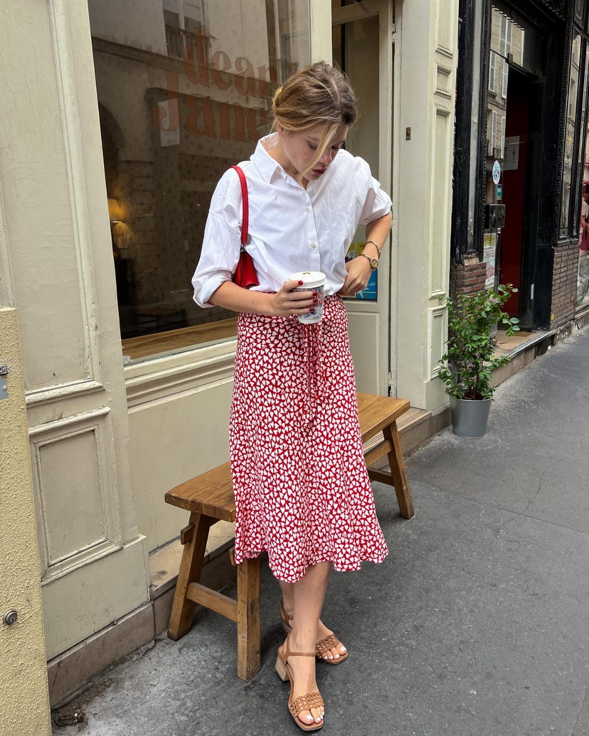 Woman wearing a white button-down shirt and red floral midi skirt on a sidewalk.