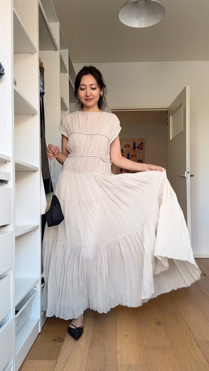 Woman wearing a flowing cream-colored pleated maxi dress and black pointed-toe heels.