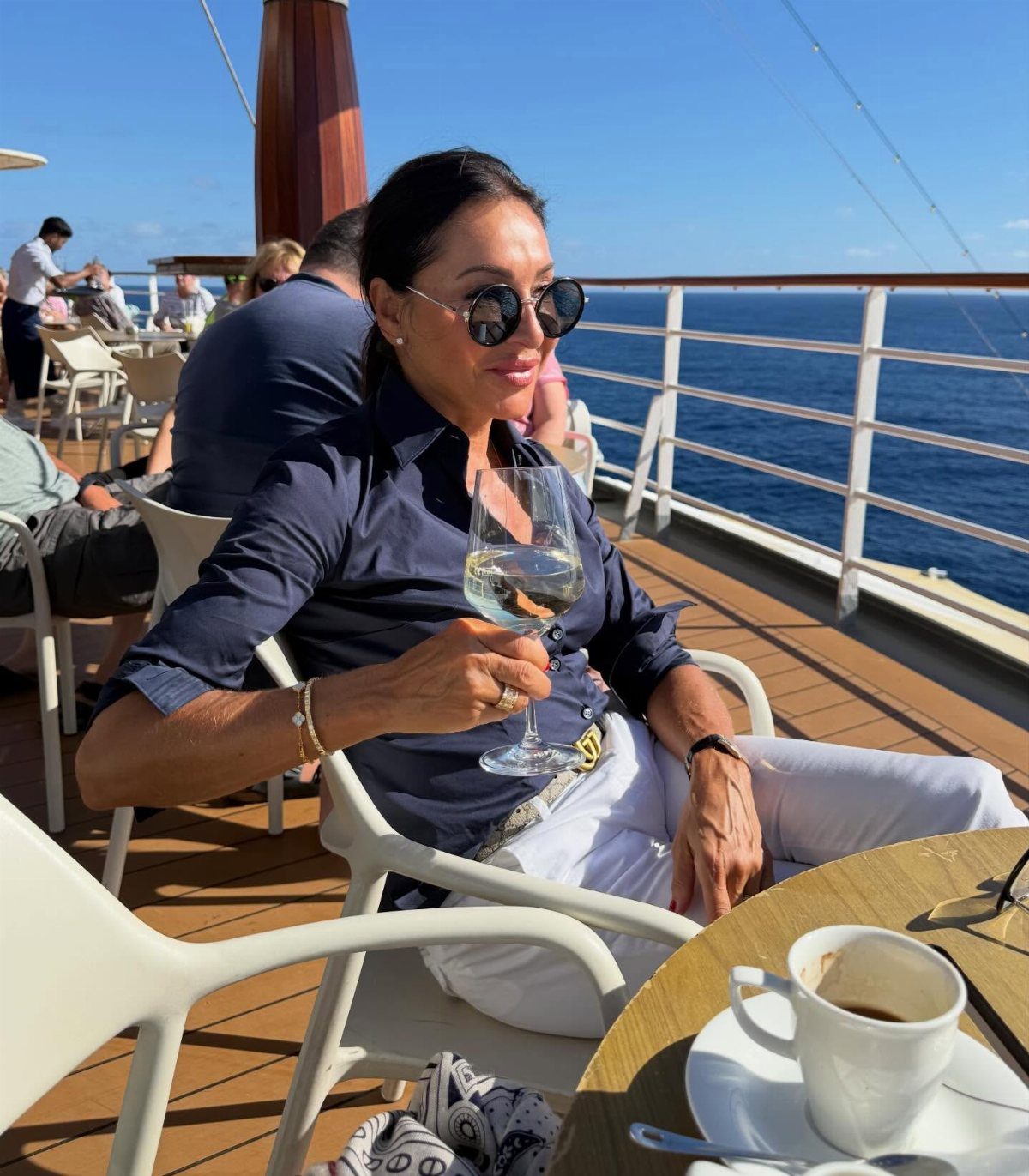 Woman in navy shirt and white pants relaxing on a cruise ship deck.