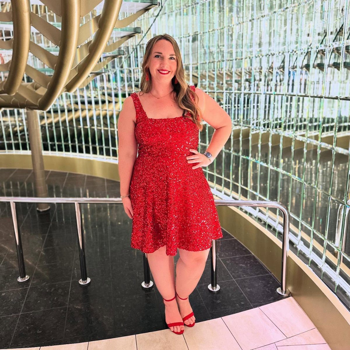 Woman wearing a short red sequin dress and red heels in a modern building.