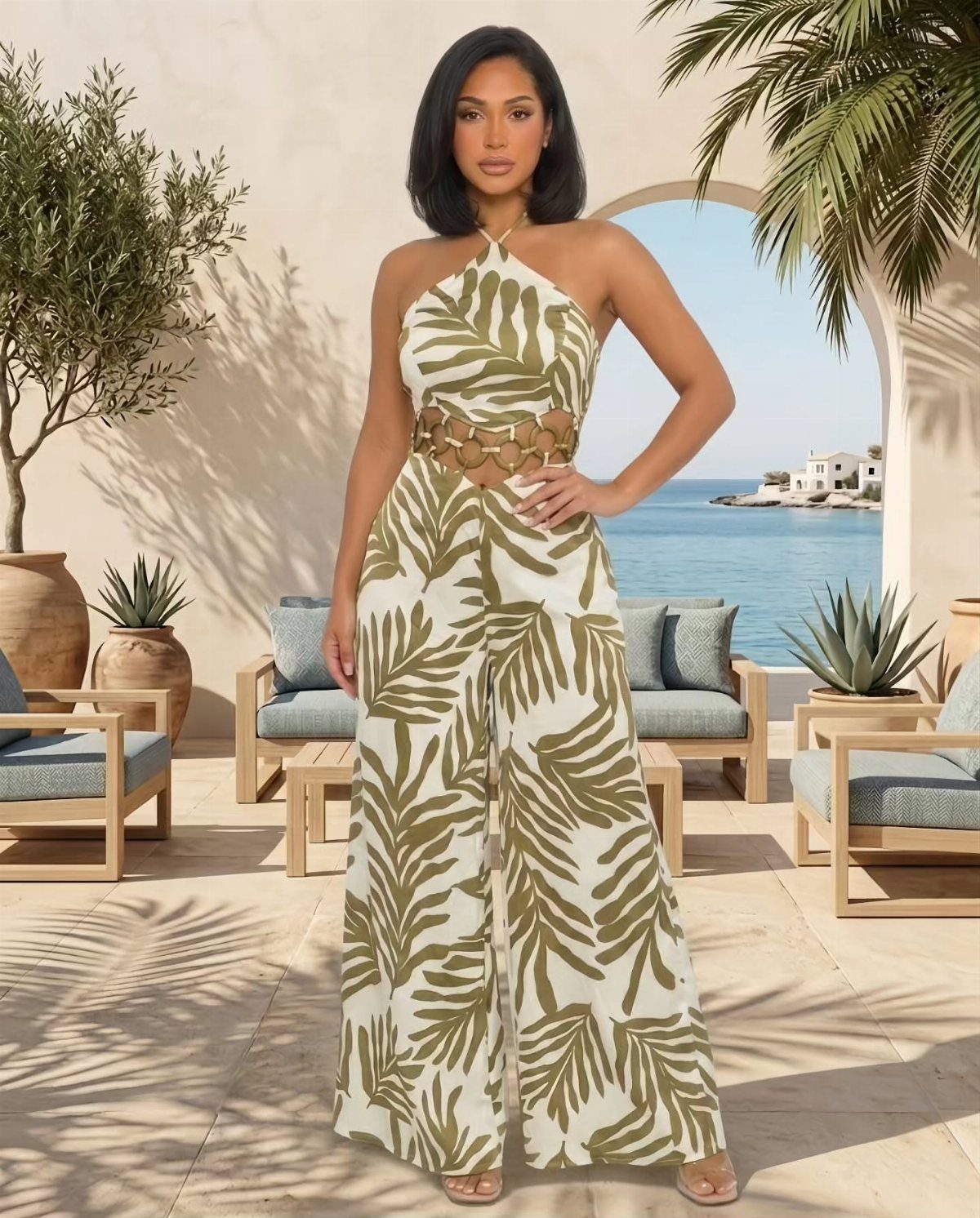 Woman in a white and green tropical print wide-leg jumpsuit on a sunny patio.