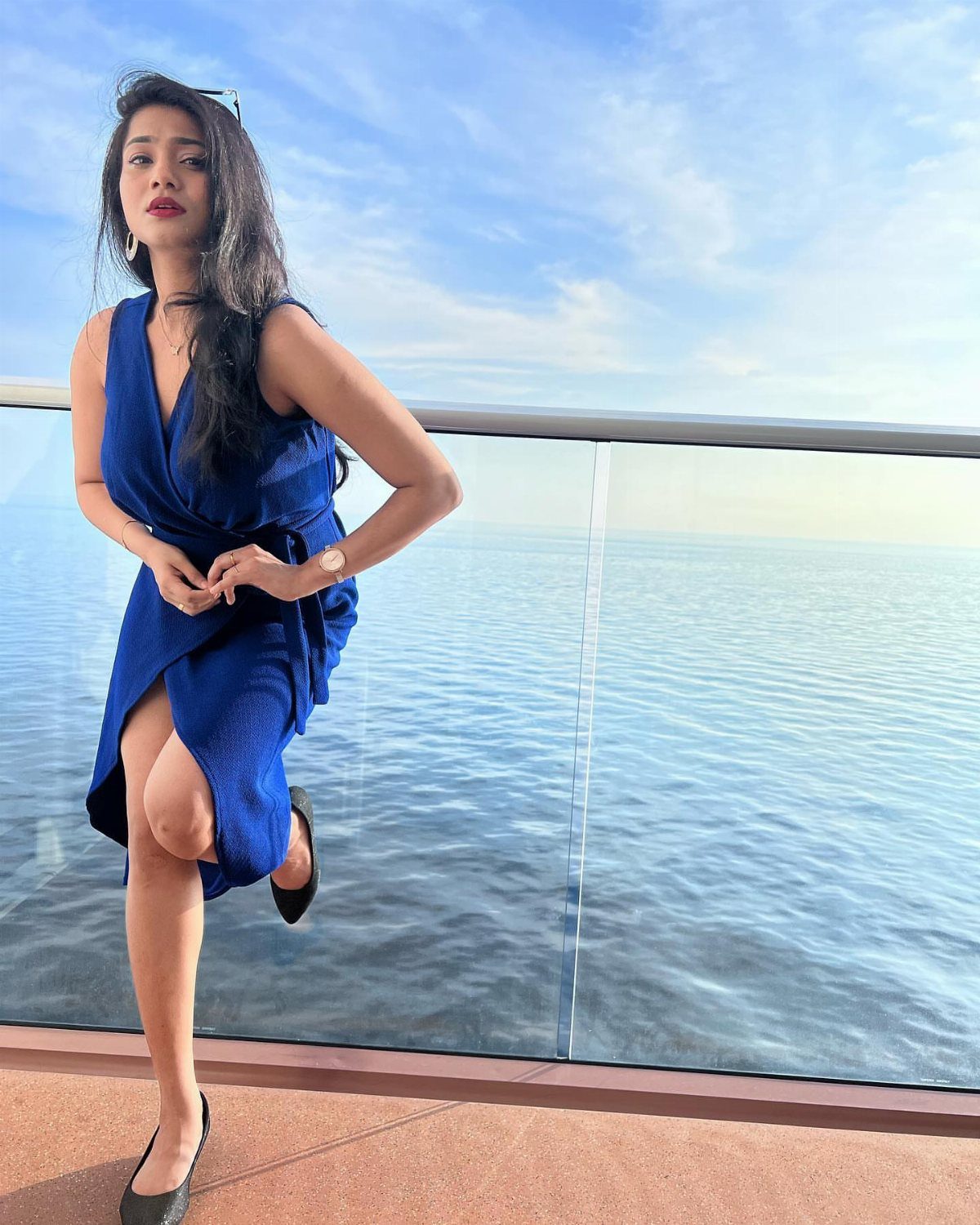 Woman in a royal blue wrap dress posing on a cruise ship deck.