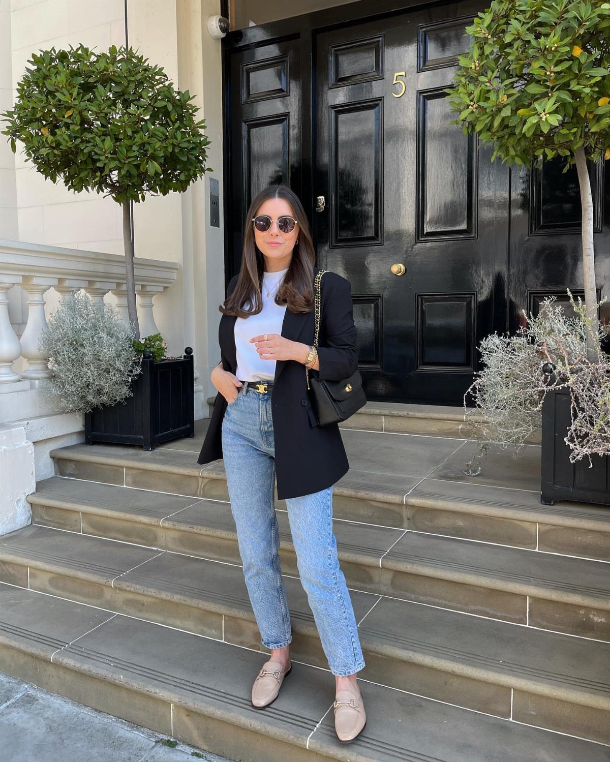 Woman wearing a black blazer, white t-shirt, and light blue jeans on stone steps.