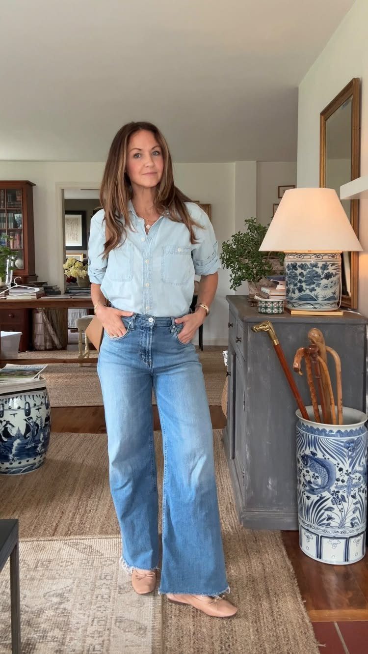 Woman wearing a light blue chambray shirt and wide-leg blue jeans in a home.