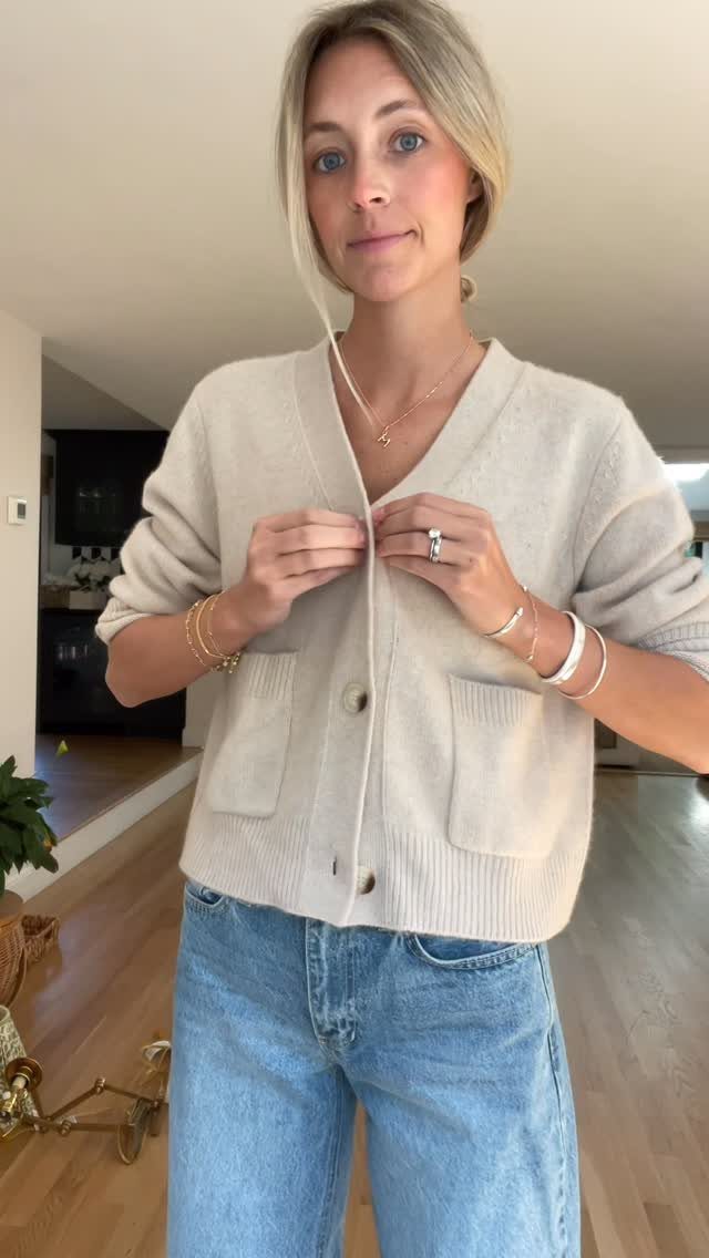 Woman wearing a cream cardigan sweater and light blue jeans in a home setting.