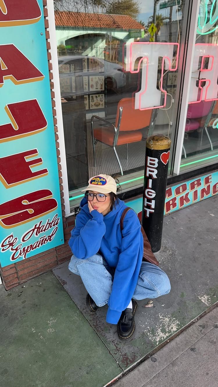 Casual Street Style: 8 Outfit Ideas for Women 5 Person in a bright blue oversized hoodie and baggy jeans crouching by a storefront.