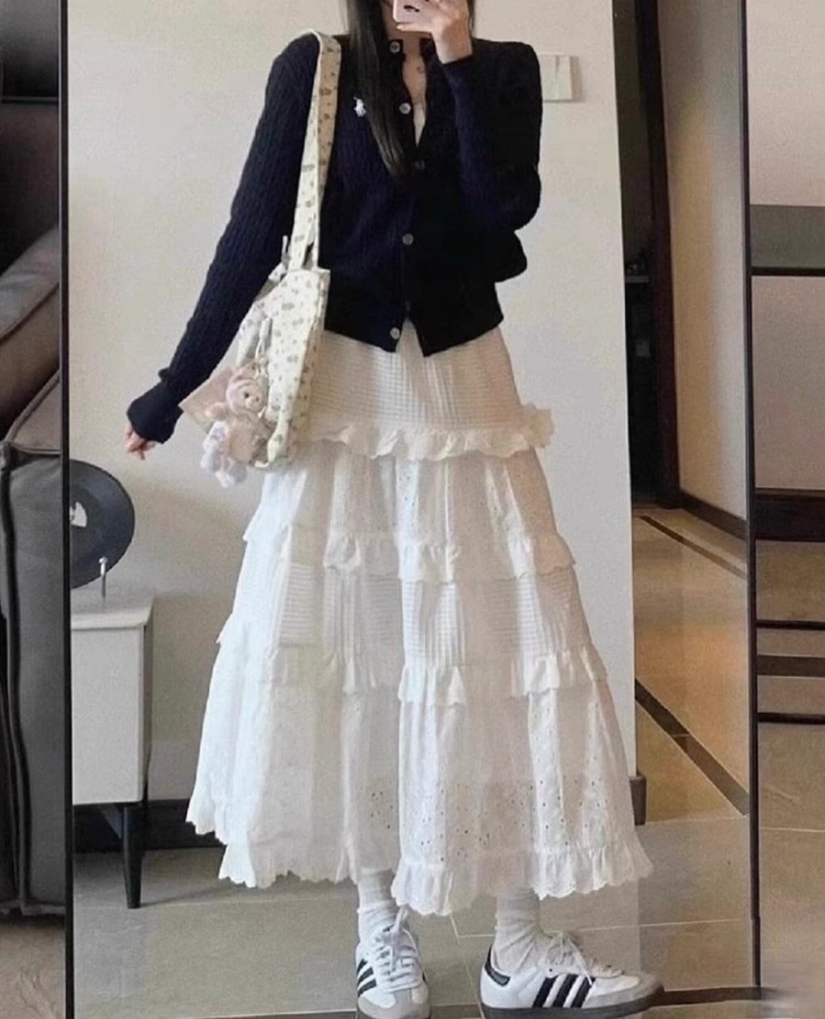 Casual Street Style: 8 Outfit Ideas for Women 8 Person in a black cardigan and tiered white lace skirt posing for a mirror selfie.